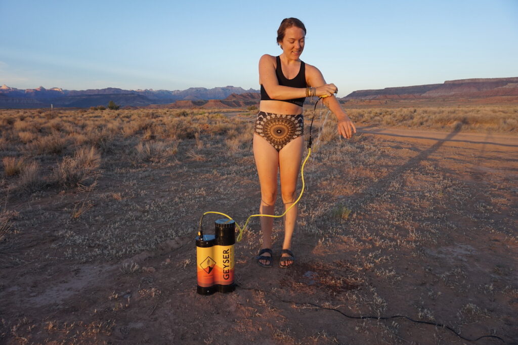 一名妇女正在用间歇泉便携式淋浴系统冲洗。她在犹他州南部的沙漠里。