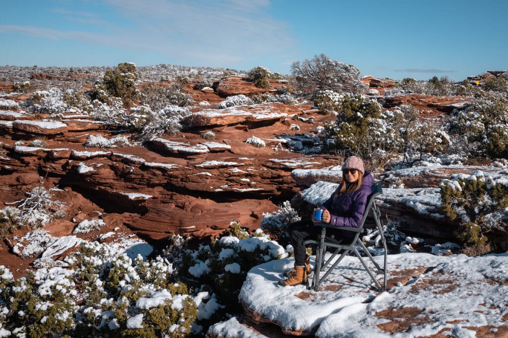 在犹他州摩押，一名妇女坐在雪人露营椅上，周围是白雪覆盖的红色岩石