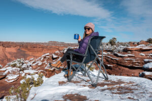 女子坐在雪人步道的营地椅子上，在一个雪景，在犹他州的红岩位置