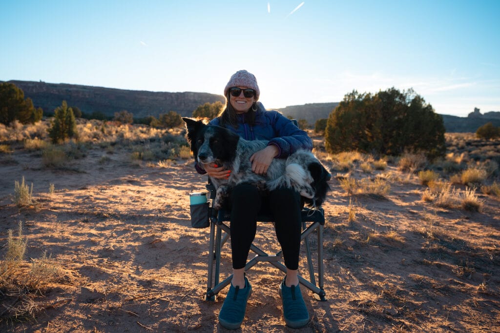 一个女人坐在YETI Trailhead露营椅上，对着镜头微笑，她的腿上躺着一只狗