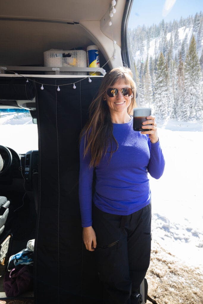 穿着Icebreaker Oasis 200贴身外套的女人在她的Sprinter面包车门口喝着aerpress的咖啡