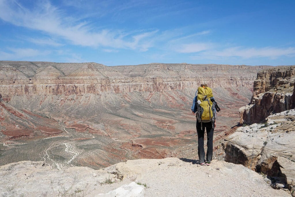 Woman standing with back to camera looking out over Arizona desert canyon carrying backpacking backpack