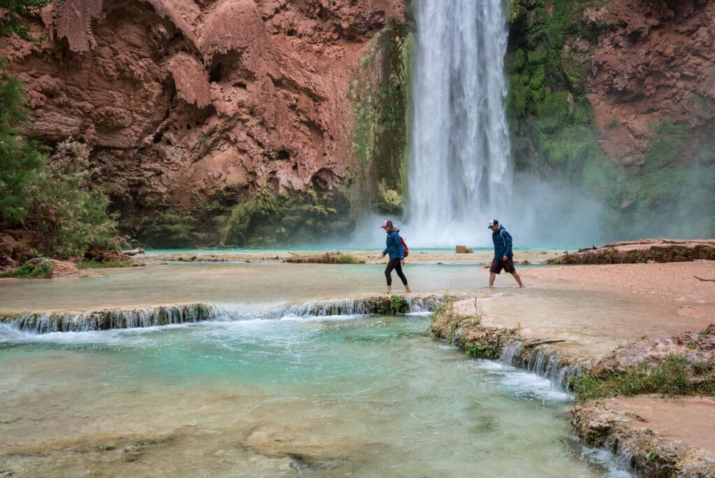 Two people walking through water at base of Havasu Falls