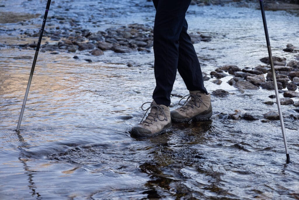 一个穿着防水登山靴的女人走过一条浅小溪的特写