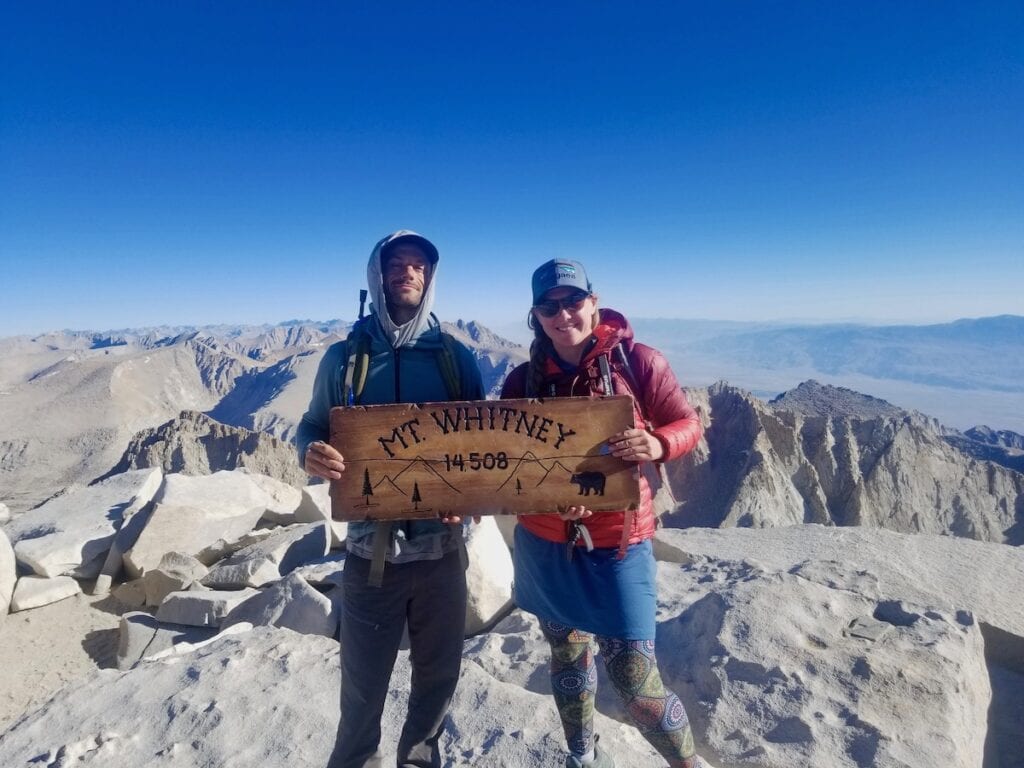 一男一女微笑着举着“惠特尼山14508英尺”的牌子