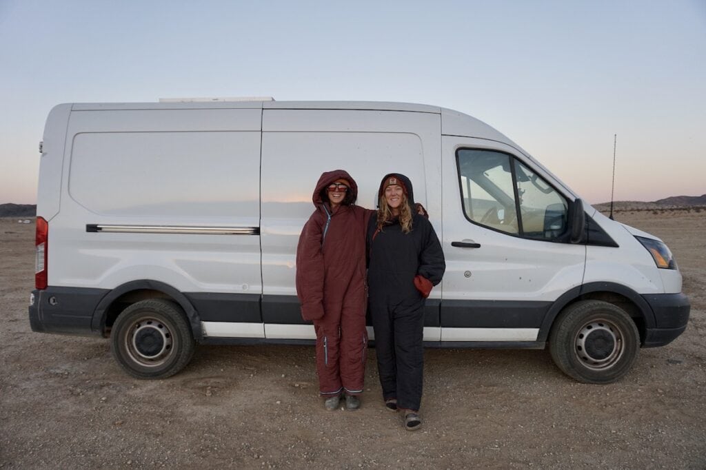 两名戴着Selk'Bag可穿戴睡眠带的妇女微笑着站在一辆白色福特露营车旁