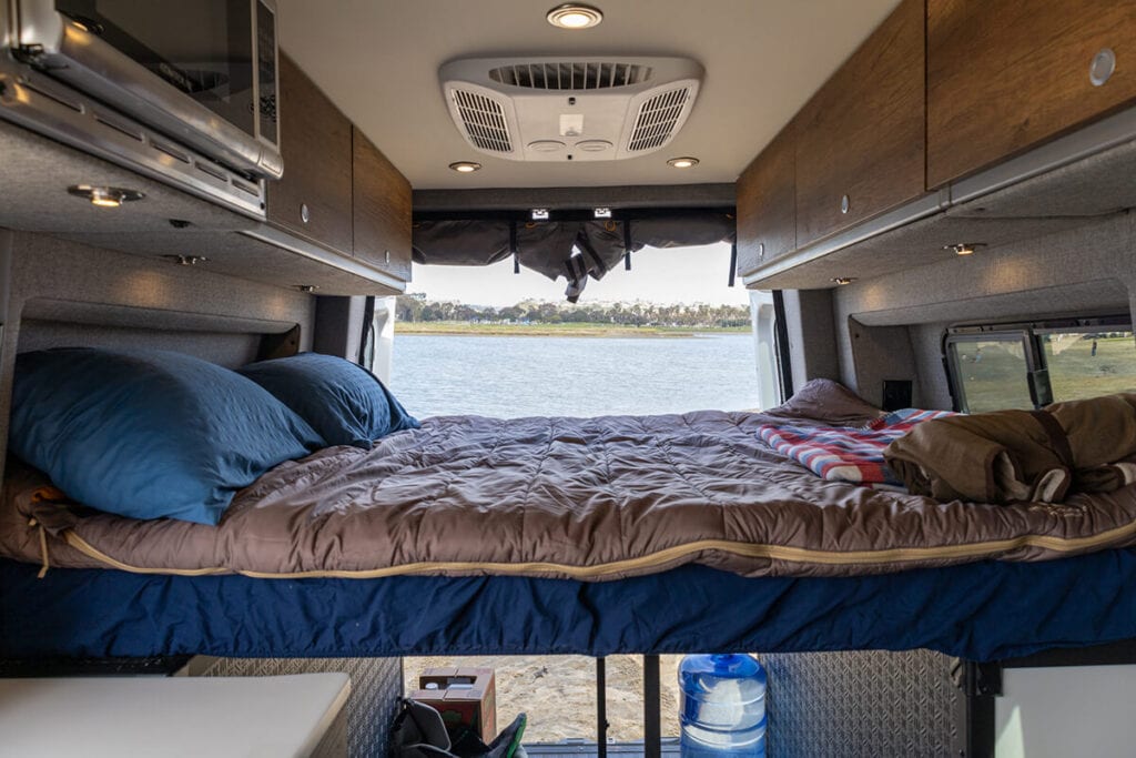 Interior view of a Storyteller Overland sprinter campervan looking out the back showing the bed made with pillows and a double sleeping bag