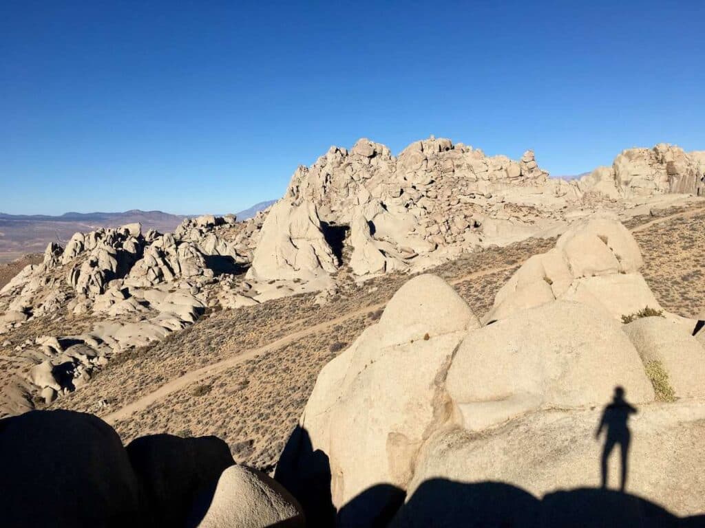 A person standing on top of a rock formation in the desert. The person's shadow is casting a long shadow over the rocks