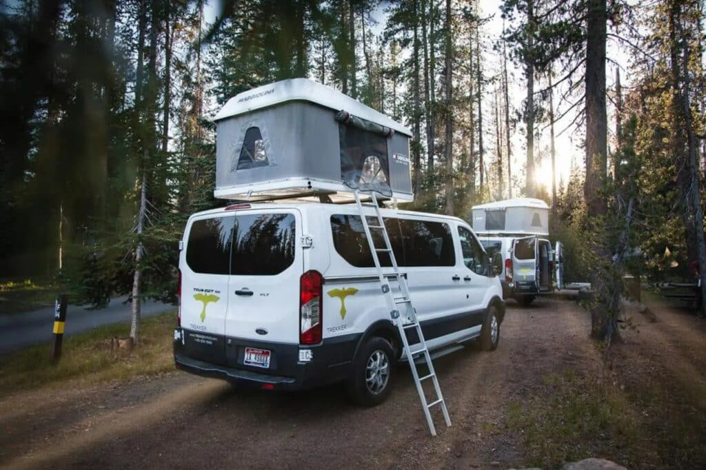 Trekkker Vans camper van rental set up at a forrested campground with a pop up rootop tent