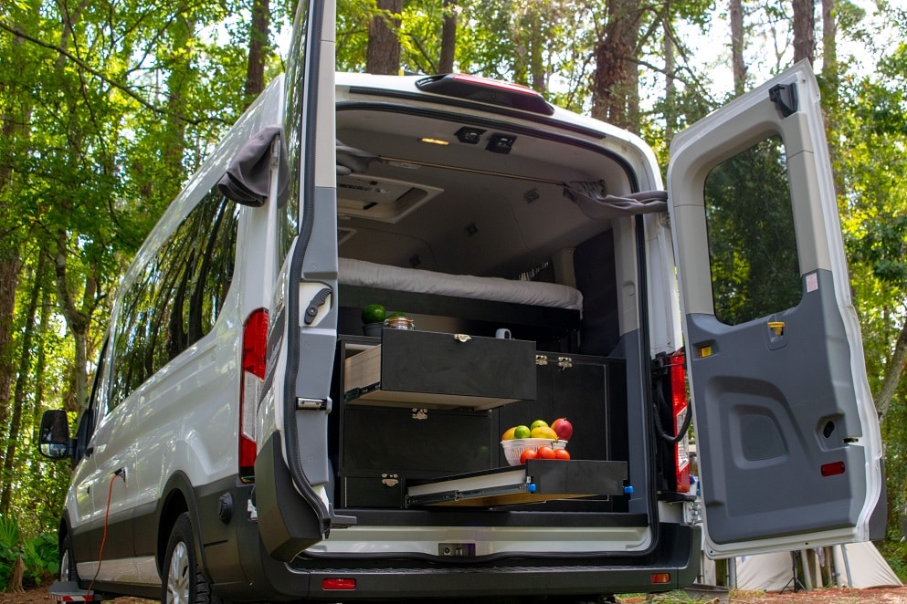 A Dodge Promaster campervan rental available through Ondevan showing the interior through the back doors with a bed and kitchen